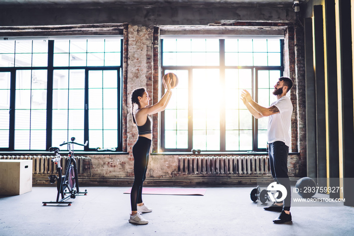 Cheerful young male and female athletes having warming exercises on workout in modern designed gym, 