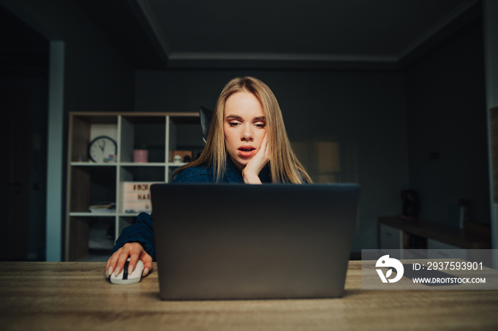 Surprised woman sitting at the table at home. sleeping and using internet on laptop with shocked fac