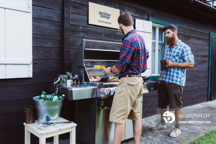 Two men cooking outdoors at barbecue station having fun