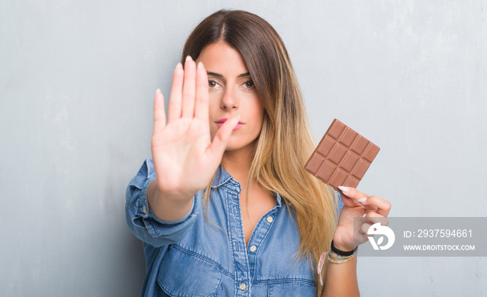 一名年轻的成年女子在灰色垃圾墙上张开手吃巧克力棒，用ser做停止手势