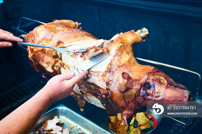 Chef Hands cutting whole grilled pork for steaks with knife. Pig grilled traditional coal and fire. 