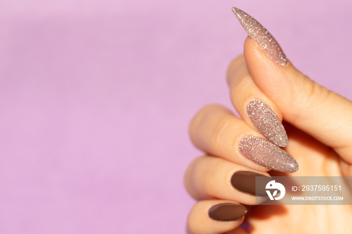 Girl`s hand with a beautiful manicure in brown and shimmer color on a purple background