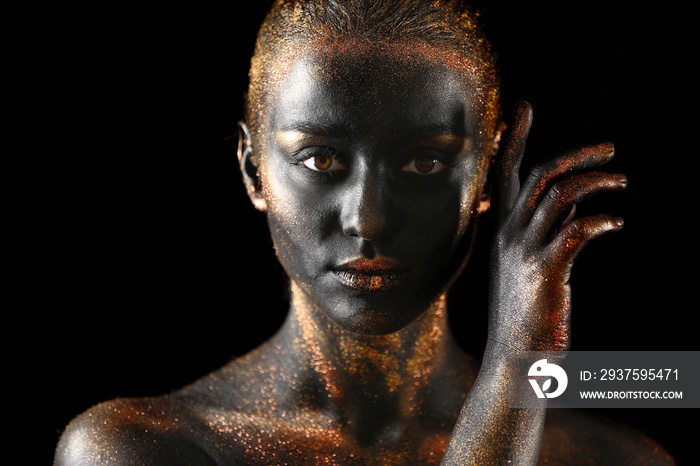 Portrait of beautiful young woman with dark paint and sparkles on her body, black background