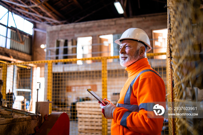 Factory workman in hard hat holding tablet computer and checking production in manufacturing factory