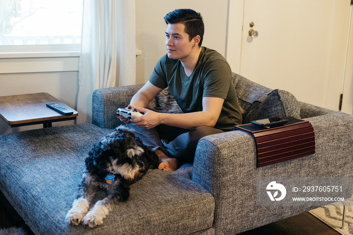 A transgender man plays video games alongside his dog.