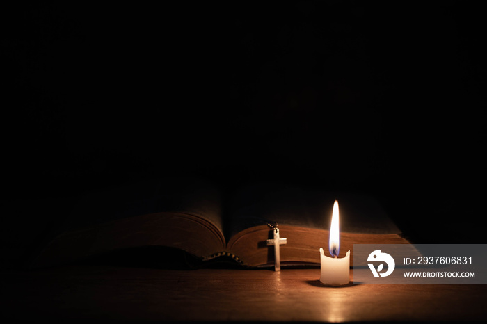 Cross with bible and candle on a old oak wooden table.