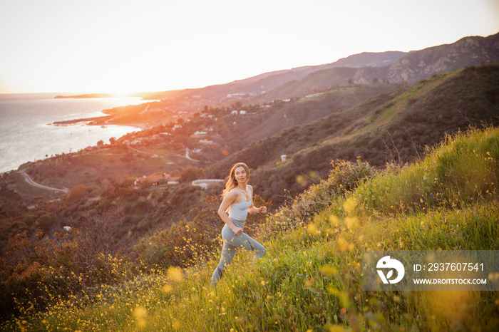 Carefree young woman wearing sports clothing while walking on mountain during sunset