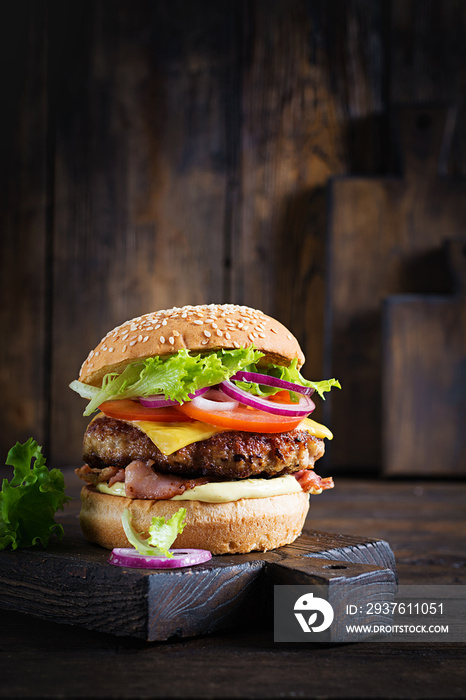 Hamburger with bacon, turkey burger meat, cheese, tomato and lettuce on wooden background. Tasty bur