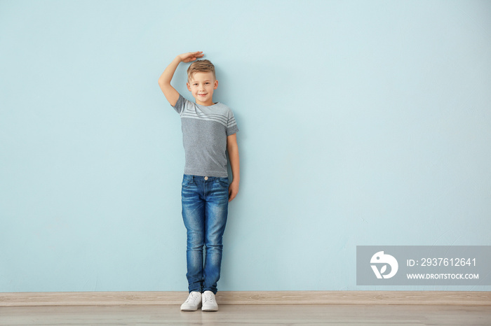 Cute little boy measuring height near color wall