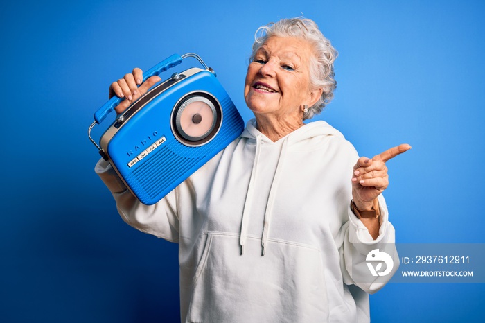 高级美女拿着老式收音机站在孤立的蓝色背景上，非常开心