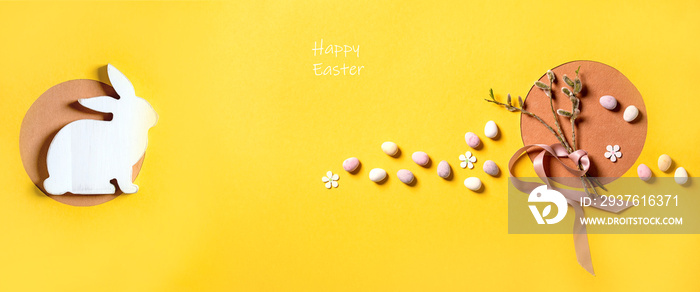 Easter greeting card with blossom willow branches, colorful candies and white rabbit on bright orang