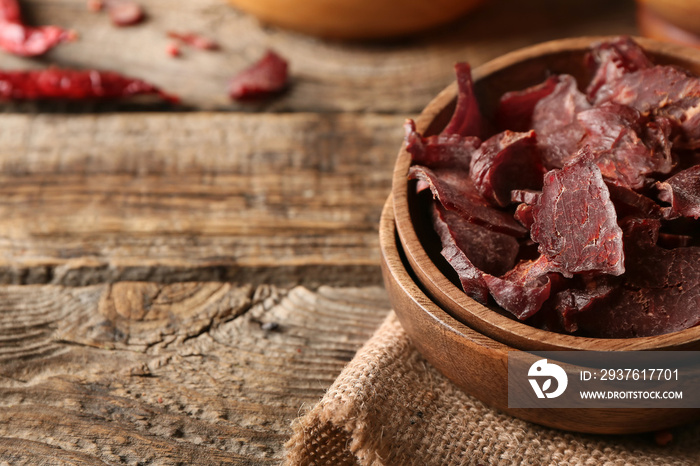 Plates with spicy beef jerky on wooden background