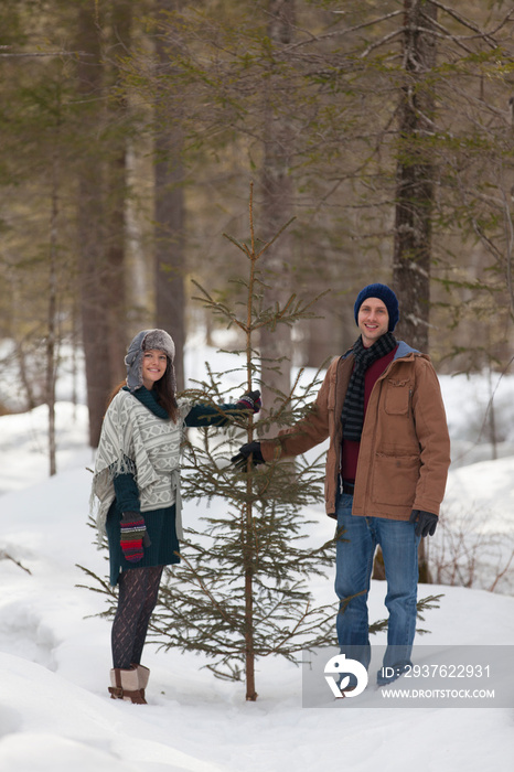 Portrait happy couple with Christmas tree in snowy woods