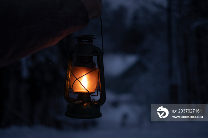 someone with a kerosene lamp in his hand walks through the snowy forest at night to his house in the