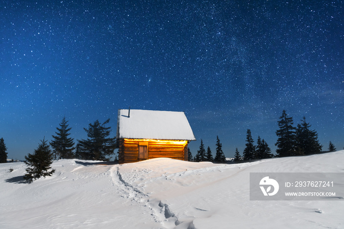 Fantastic winter landscape with wooden house in snowy mountains. Smoke comes from the chimney of sno