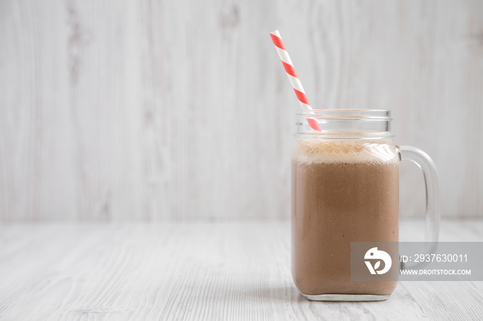 Homemade coffee, oat and banana smoothie in a glass jar mug on a white wooden surface, side view. Sp