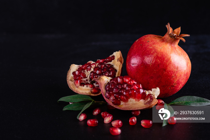 Red juice pomegranate on dark background. Ripe pomegranate with leaves on a dark background