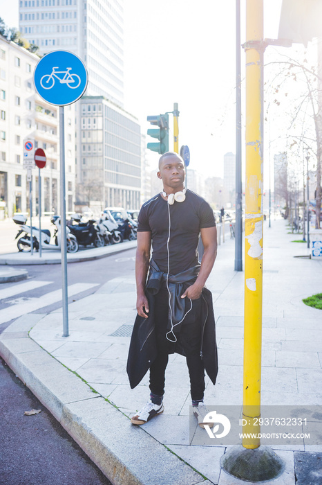 Young man standing by road, headphones around neck, looking away