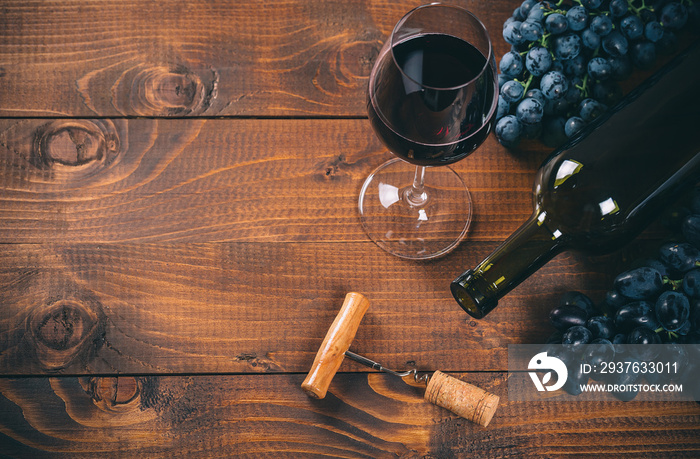 Bottle and glass of red wine, grape, corkscrew and cork on wooden background