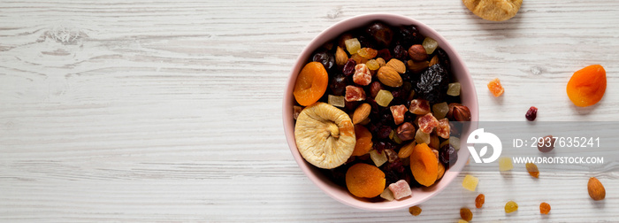 Dried fruits and nut mix in a pink bowl on a white wooden surface, top view. Overhead, from above, f