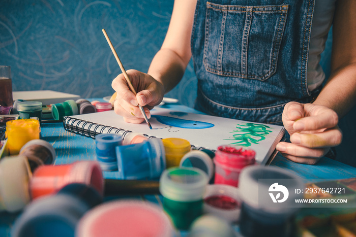 Pretty smiling young woman drawing a picture with poster paint