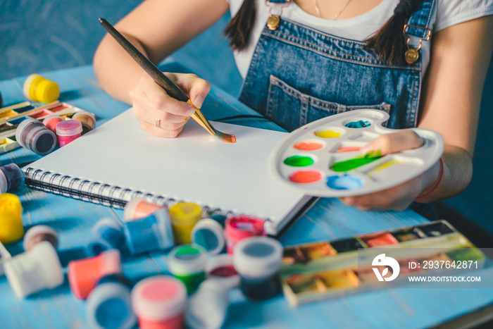 Pretty smiling young woman drawing a picture with poster paint