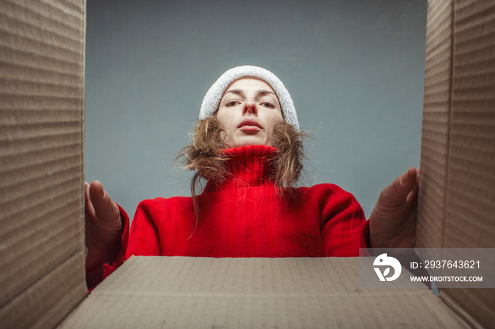 戴着圣诞老人帽子、穿着红色毛衣的女孩看着盒子里的东西。打开的概念