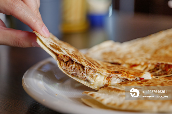 用手近距离拿起一块墨西哥著名食物Quesadilla，放在白色盘子上。