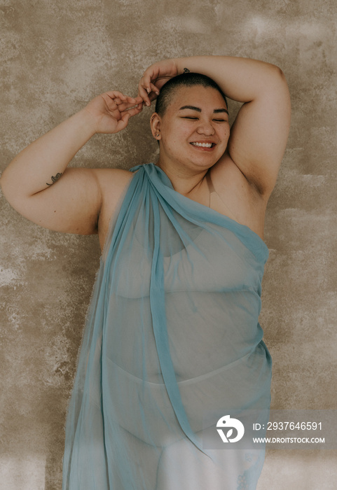 plus size filipino woman with shaved head wrapped in blue fabric smiling and laughing