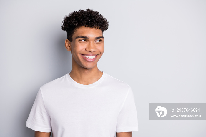 Portrait of brunet optimistic curly guy look empty space wear white t-shirt isolated on grey color b