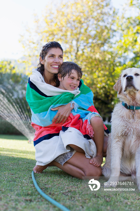 Happy mother and son wrapped in towel with dog in backyard