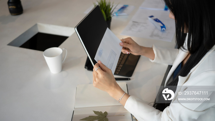 Close up view of businesswoman sitting at her office desk and holding envelope.