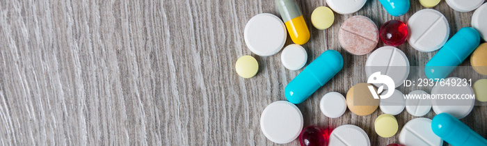 Banner of A lot of colorful medication and pills from above on grey wooden background.