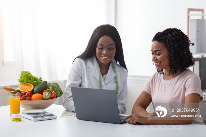 Smiling female doctor and patient using laptop in clinic