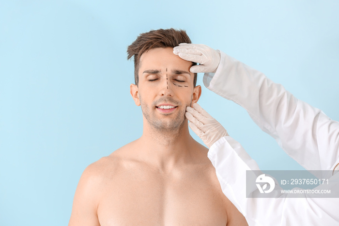 Plastic surgeon touching face of young man on color background