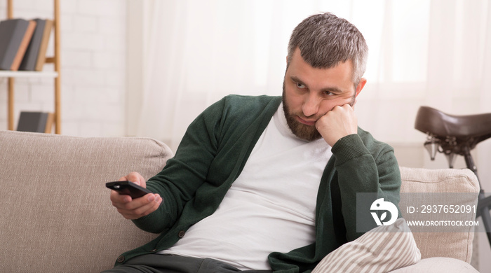 Bored man switching channels on TV on weekend