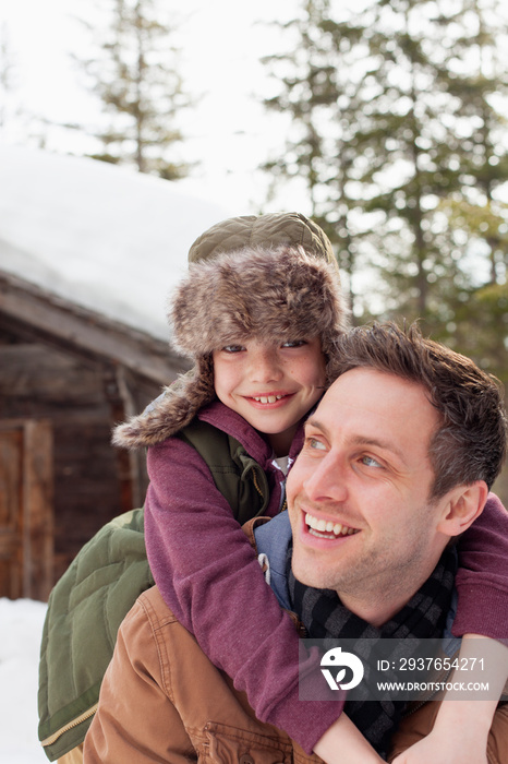 Portrait happy father and son piggybacking outside cabin