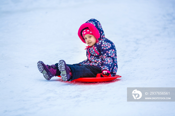 Cute litter girl sliding down on the snow mountain