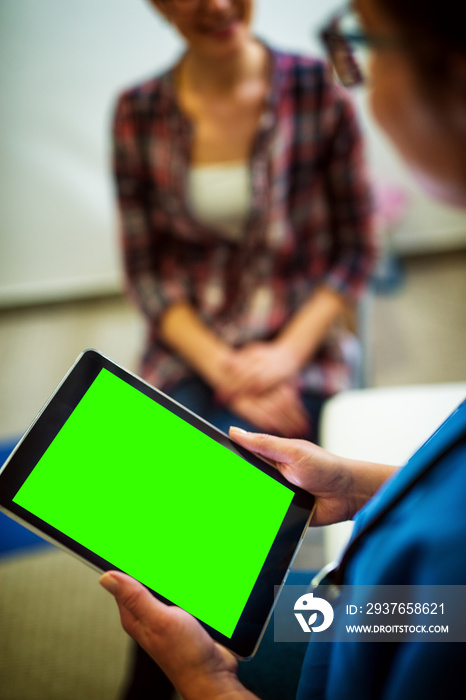 专业中年护士拿着平板电脑的后视图，平板电脑上有空白可编辑的绿色屏幕。