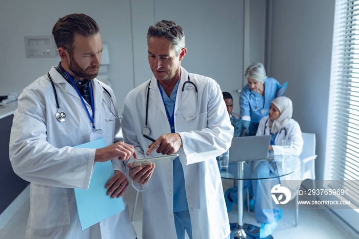 Male doctors discussing over digital tablet at hospital