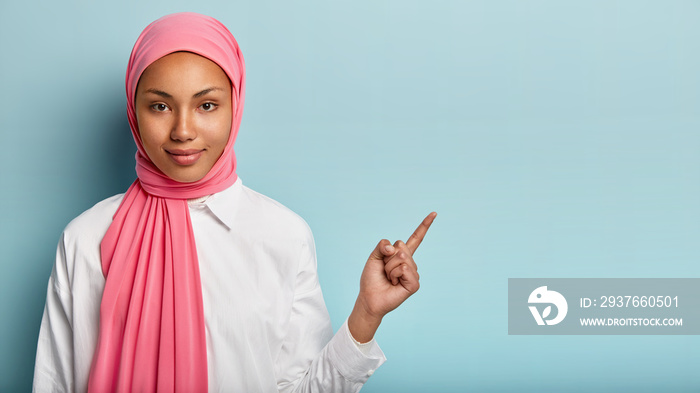 健康的穆斯林妇女用食指指着旁边的空闲空间，没有化妆，裹着