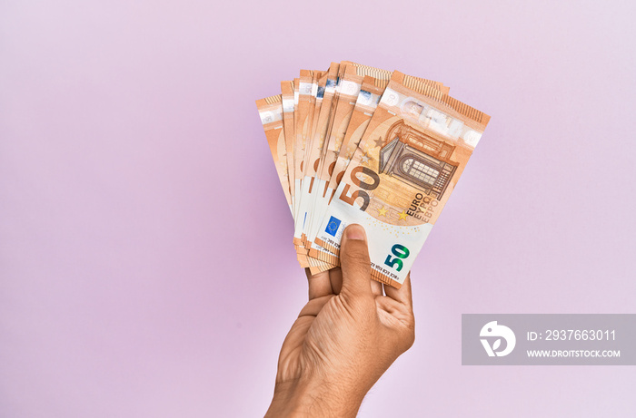 Hispanic hand holding 50 euro banknotes over isolated pink background.