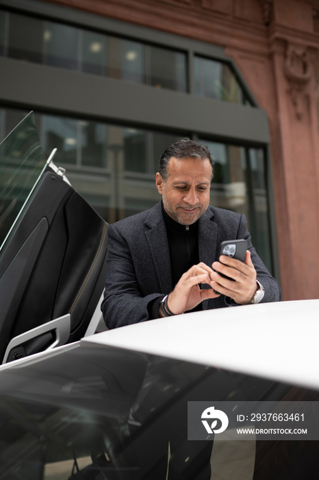 Mature man standing by luxury car and using phone