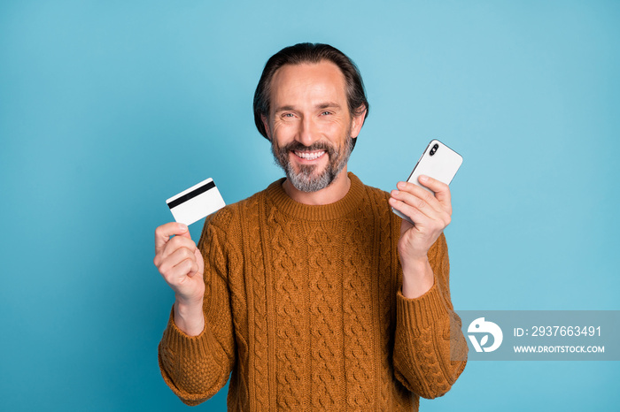 Photo of cheerful handsome guy hands hold phone debit card toothy smile isolated on blue color backg