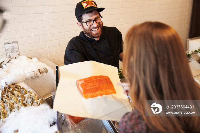 Fish vendor selling raw salmon fillet to customer