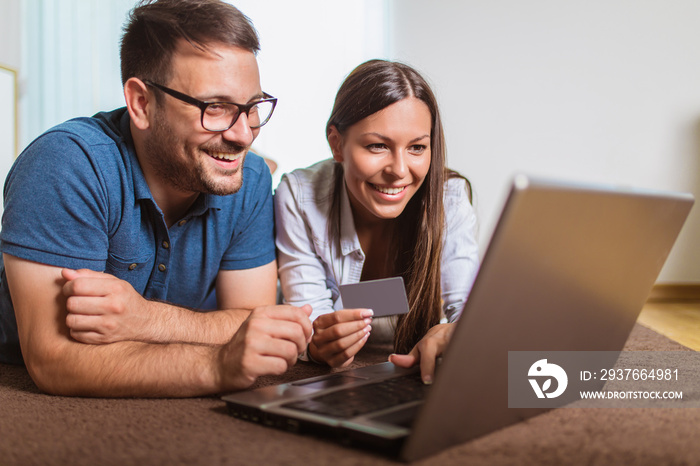 Smiling happy couple with laptop and credit or bank card shopping online at home