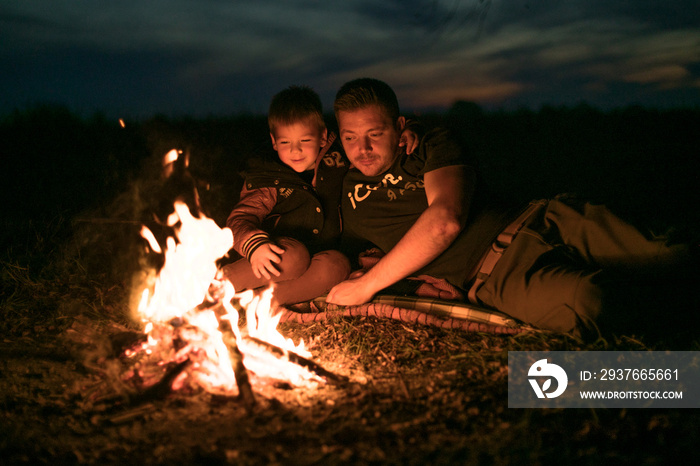 父亲和可爱的小儿子坐在森林的炉火旁。最好的朋友在一起。
