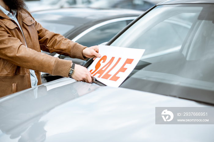 Salesperson putting sale plate on the car windshield on the open ground of a dealership, close-up vi