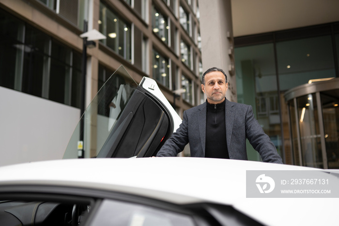 Mature man leaning against luxury car