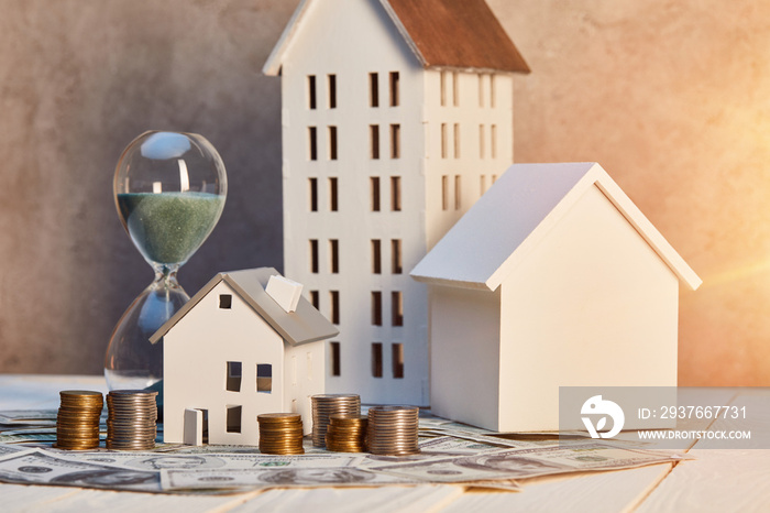 houses models, coins and cash, hourglass on white wooden table with sunlight, real estate concept